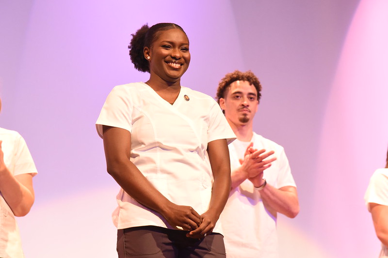 A Lincoln University nursing student smiles on stage during the Fall 2025 pinning ceremony as a fellow student applauds in the background.