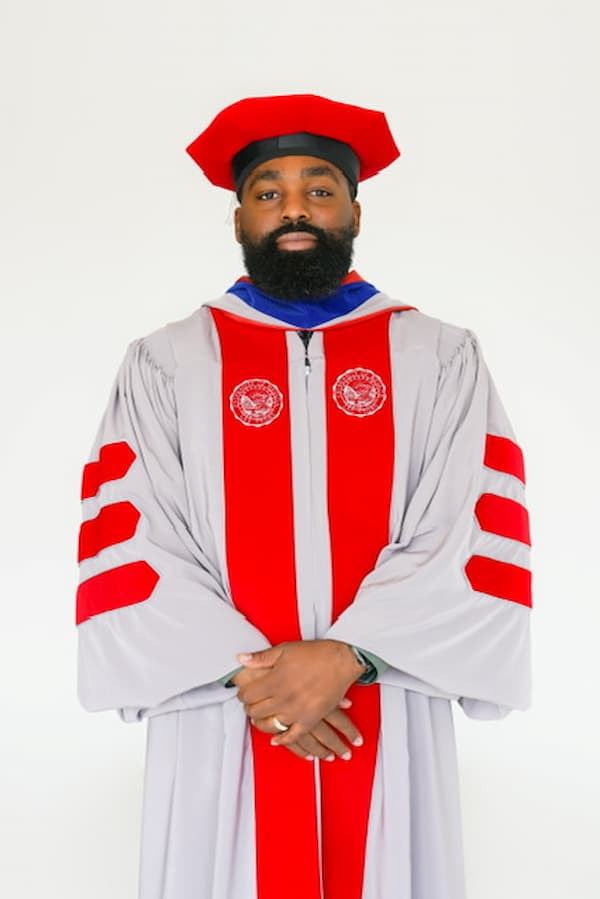 Joseph Simmons Jr. celebrates commencement at Lincoln University, raising his hands while wearing a graduation cap and gown, an Omega Psi Phi stole, and an honor sash on the stadium track.