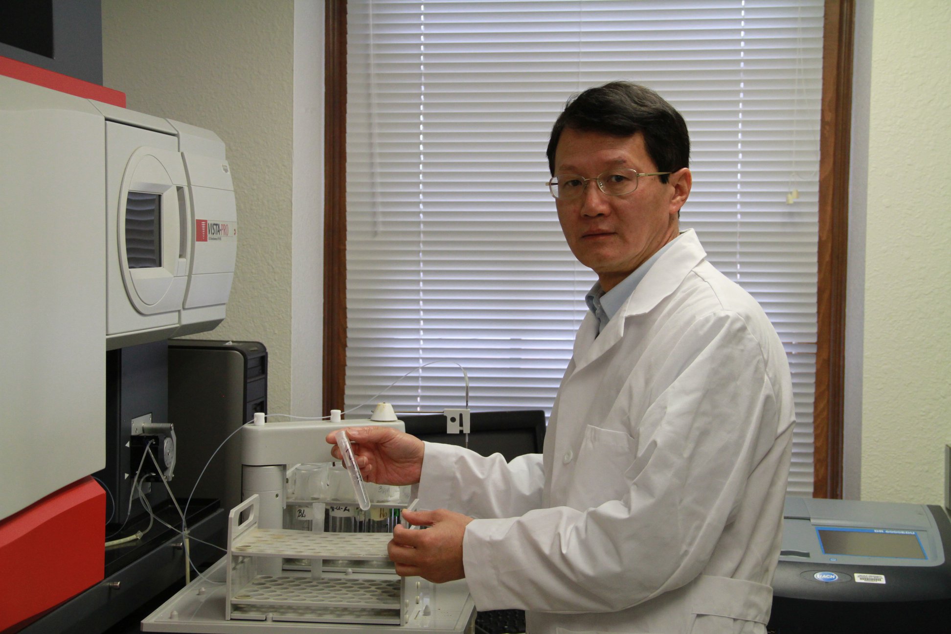 A man in a white lab coat stands working with some vials in a laboratory.