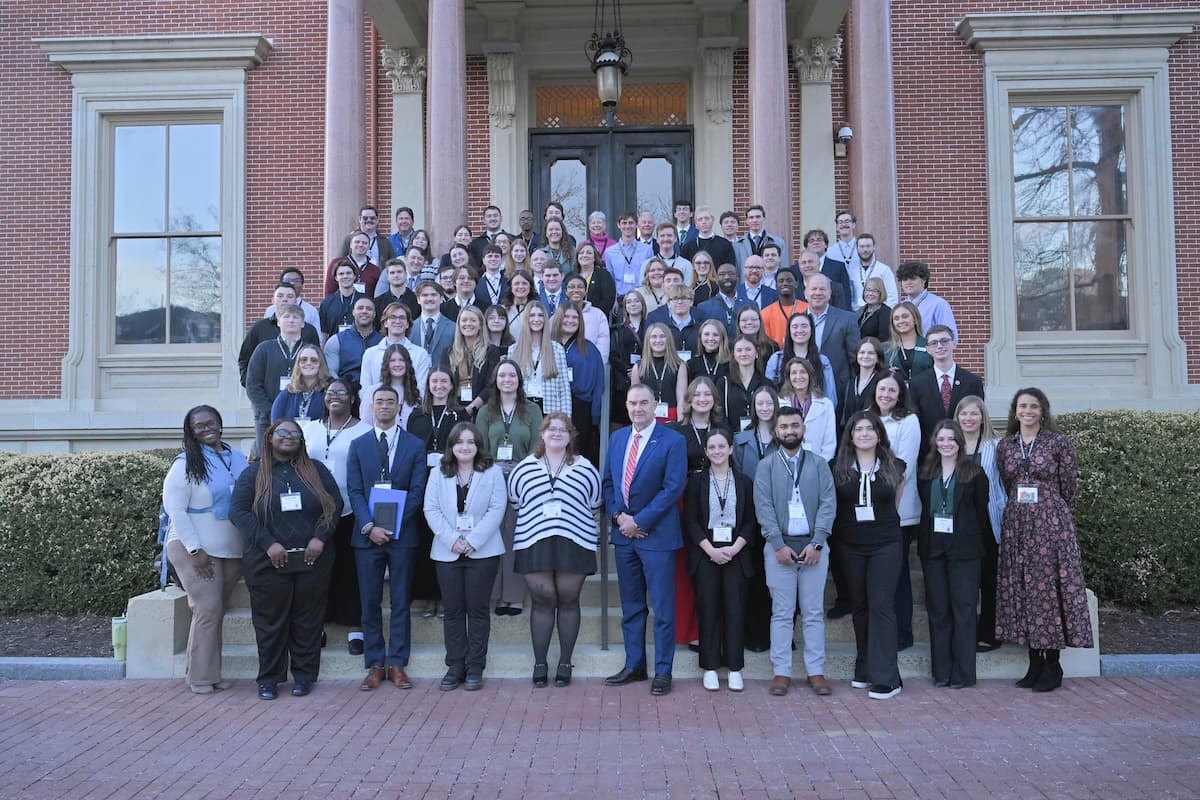 Rows of people dressed in professional clothing stand outside to pose for a photo.