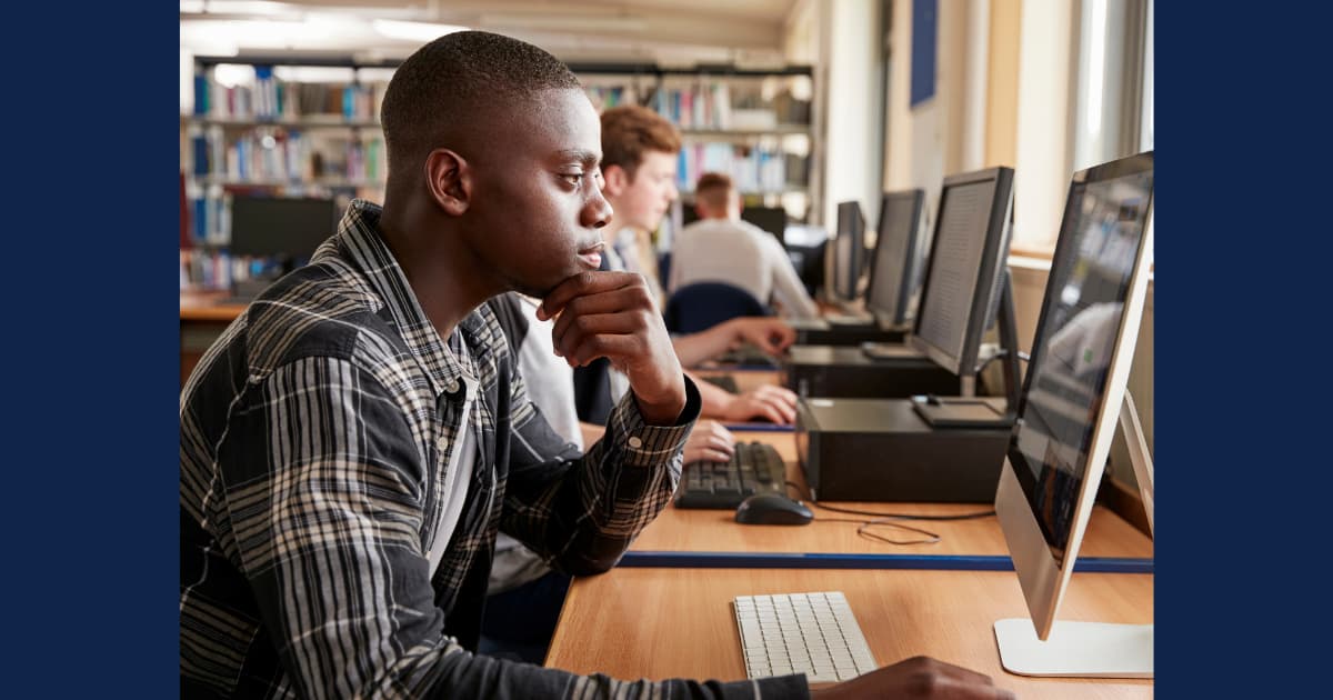 Graduate student studying at a desktop computer in a campus library computer lab, focused on academic research.