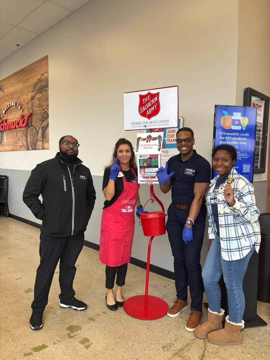 Four Lincoln University representatives stand by a Salvation Army donation container for the LU Day of Ringing in November 2025.