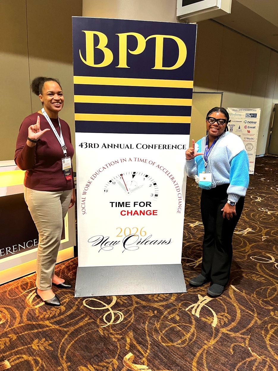 Two young women stand in front of a blue sign.