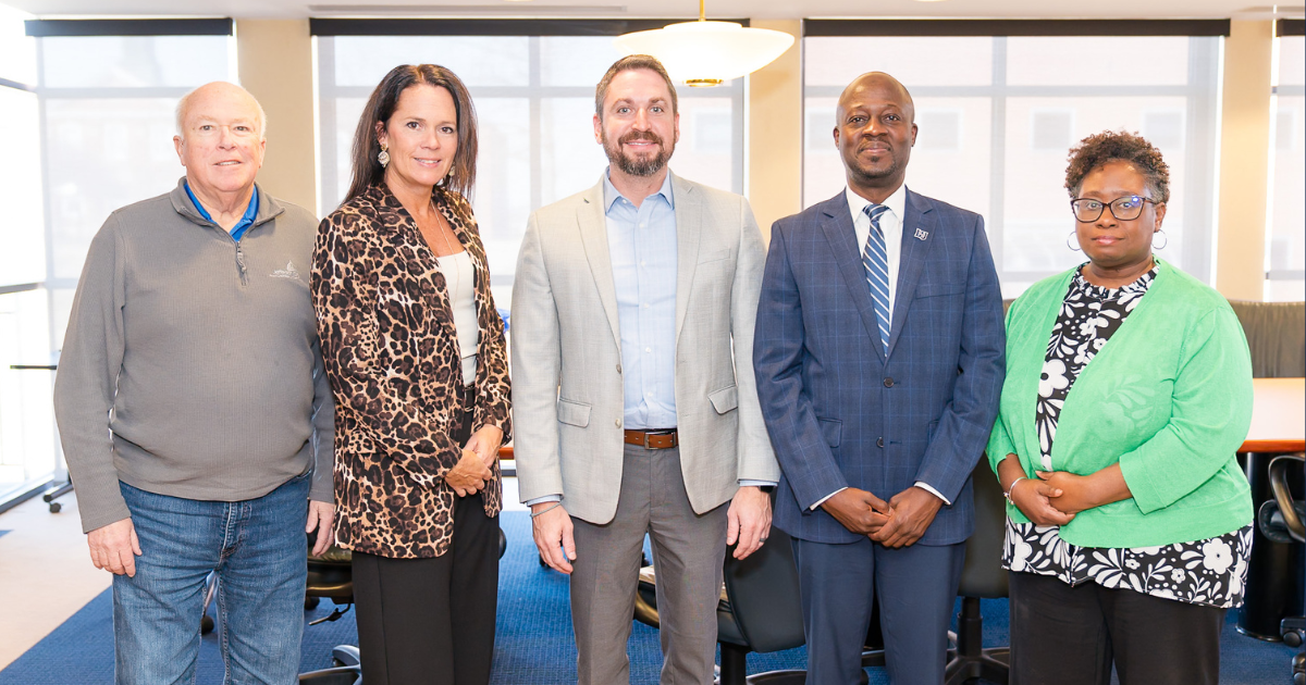 FIve people in business clothes stand in a line to smile for a photograph. 