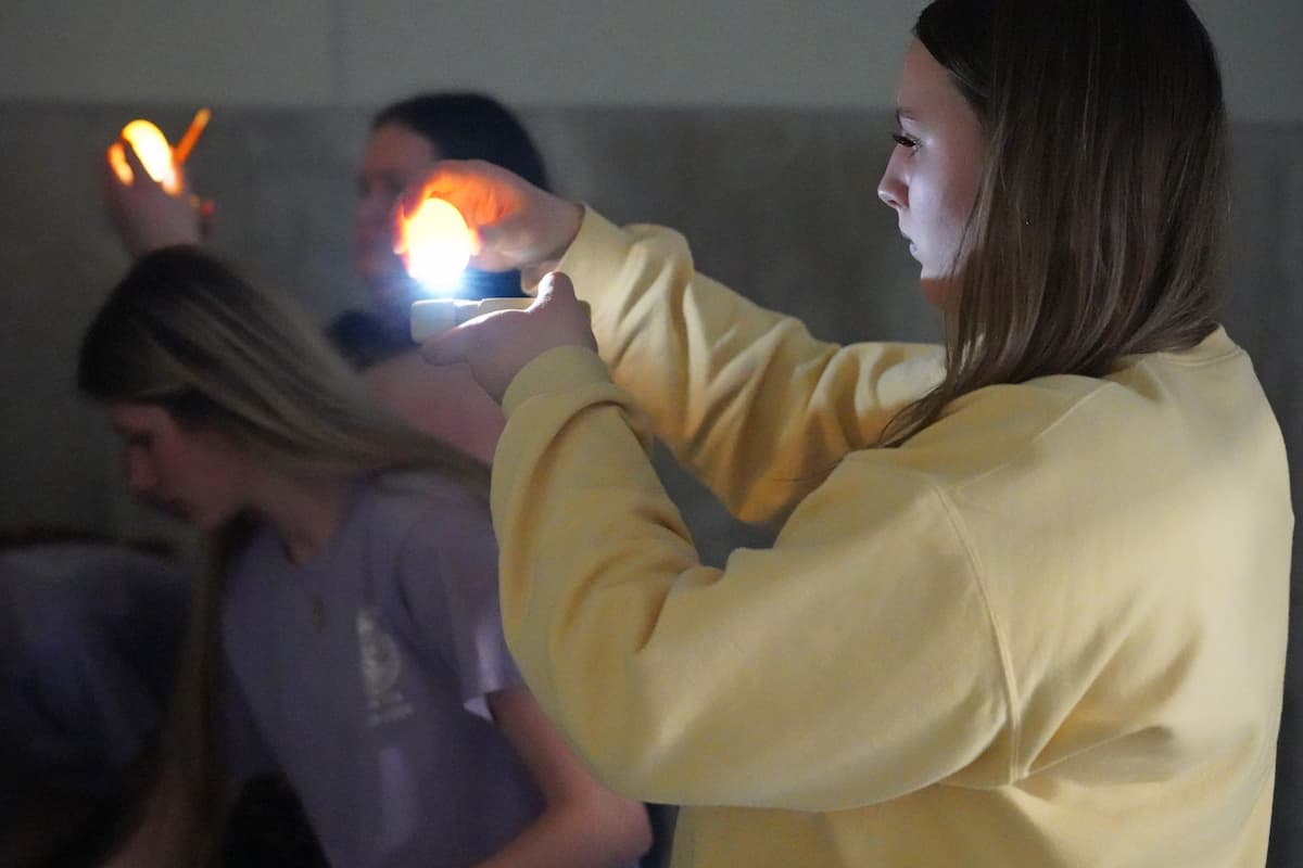 Three people in a dimly lit room, each holding a small light source up to an egg.
