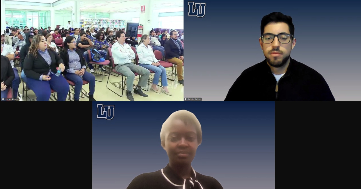 Audience members seated in a conference room watch a virtual symposium, while two presenters appear on screen during Lincoln University’s international event.