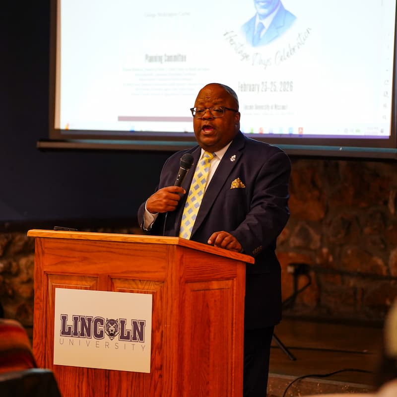 A man standing behind a lectern speaks into a microphone.