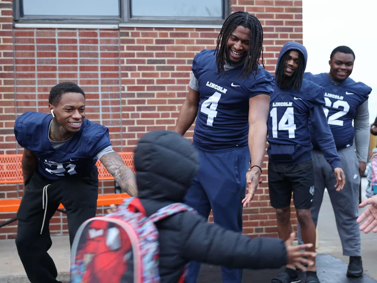 A group of LU football players high five a child as they walk into school.