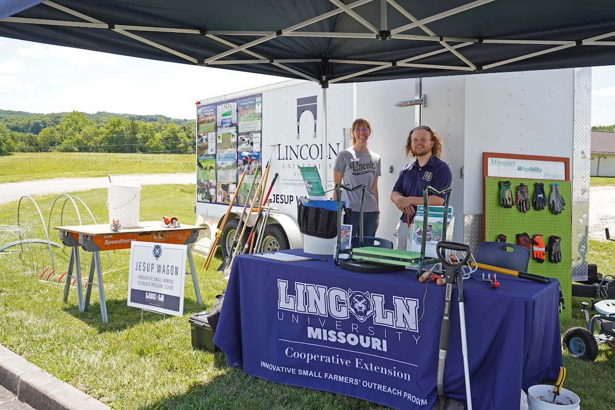 Jesup Wagon 2.0 outreach booth under a canopy with Lincoln University staff and a table displaying ergonomic farming tools and equipment.