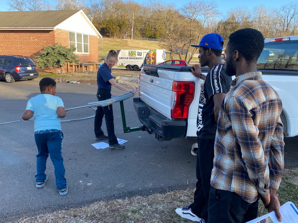 A participant bends metal conduit into a hoop for a low tunnel.