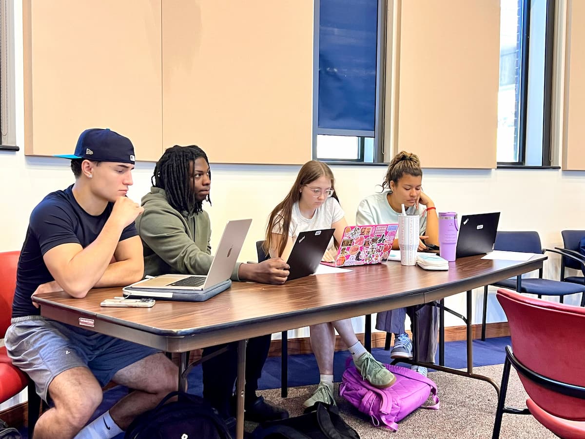 Four Lincoln University students sit at a table while working on laptops. 