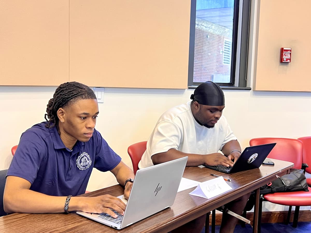 Two Lincoln University students sit at a table while working on laptops.