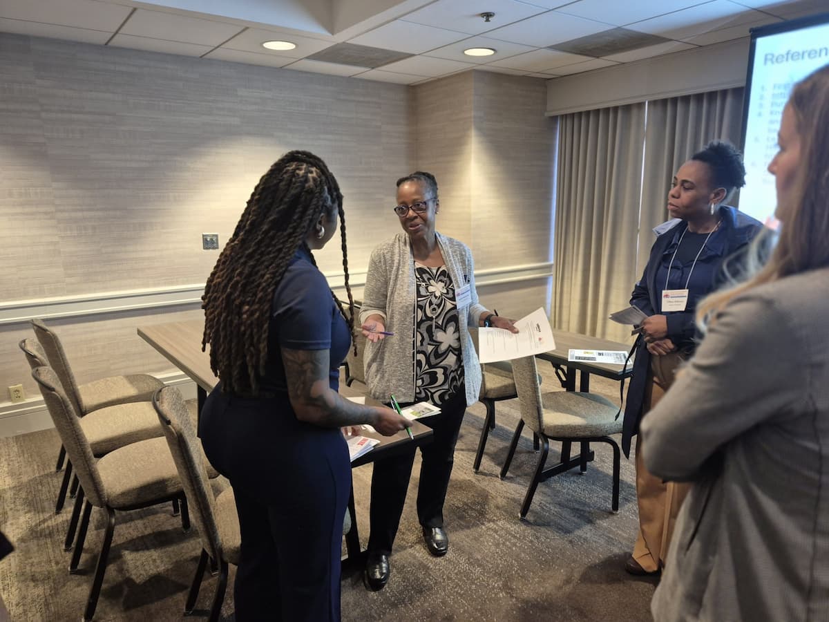 Four women stand in a group, with two of them speaking to each other.