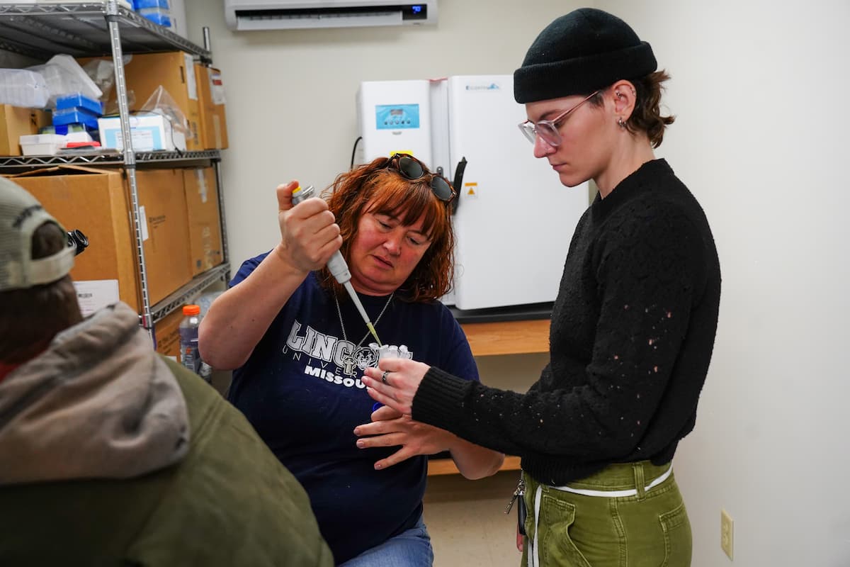 A person using a pipette to transfer liquid into a small container held by another individual.
