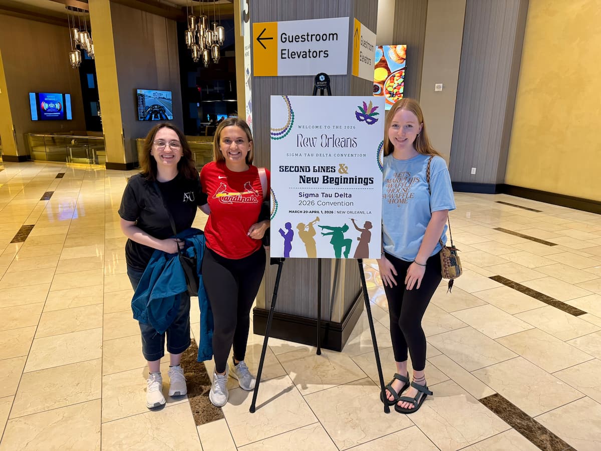 Three female Lincoln University students stand with a sign for the Sigma Tau Delta writing convention.