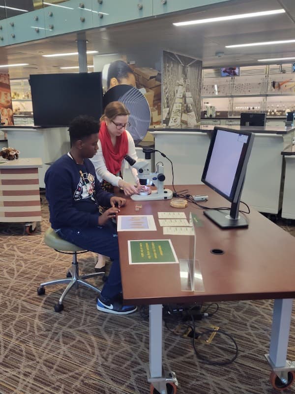 A boy and a woman look at a microscope on a table together.