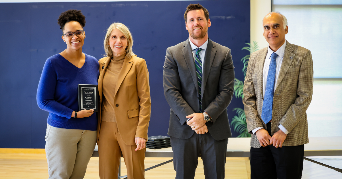 Two women and two men stand in a line while holding an award in business clothing.