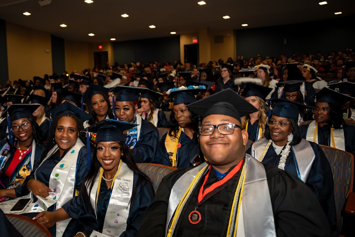 Lincoln University students in graduation regalia sit in the auditorium smiling for the camera.