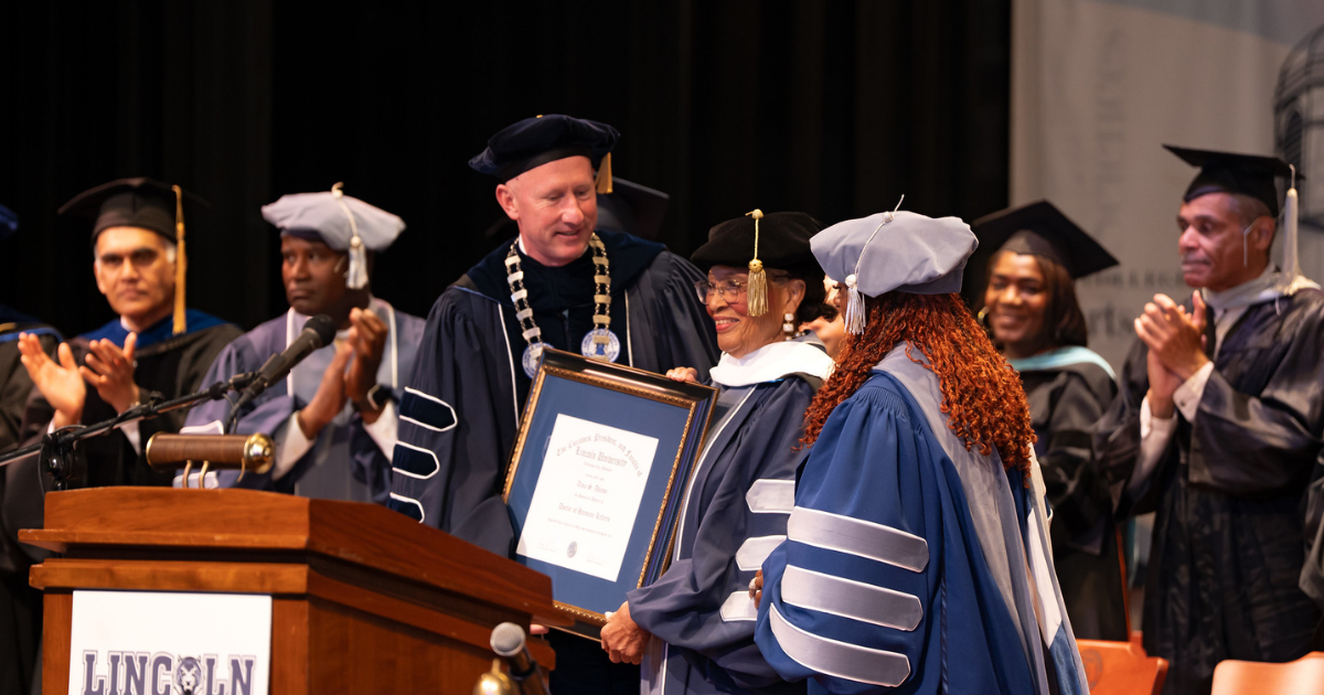 Lincoln University officials present an honorary degree during the 2026 commencement ceremony as faculty and graduates applaud.