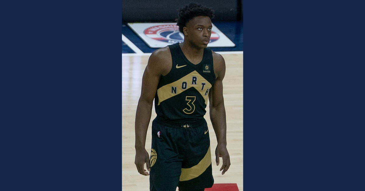 A young man in a black basketball uniform plays on the court.