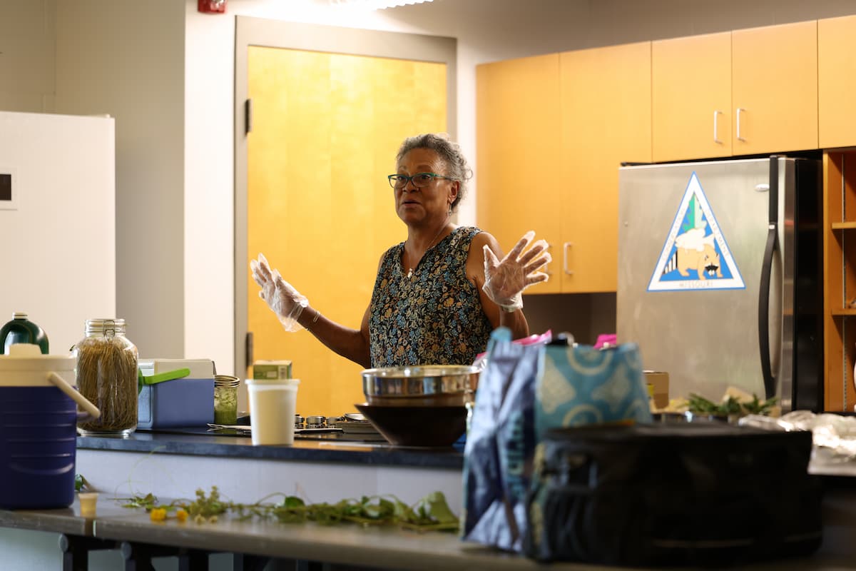 Tina Wurth stands behind a kitchen counter wearing gloves during a Native Plant Academy cooking demonstration.
