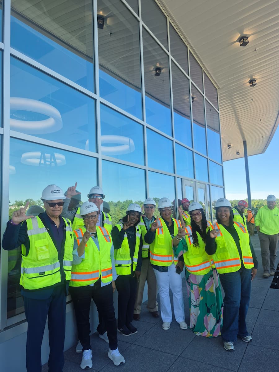 The Alumni Council stands in hard hats and bright yellow vests while touring the Health and Security Sciences building.