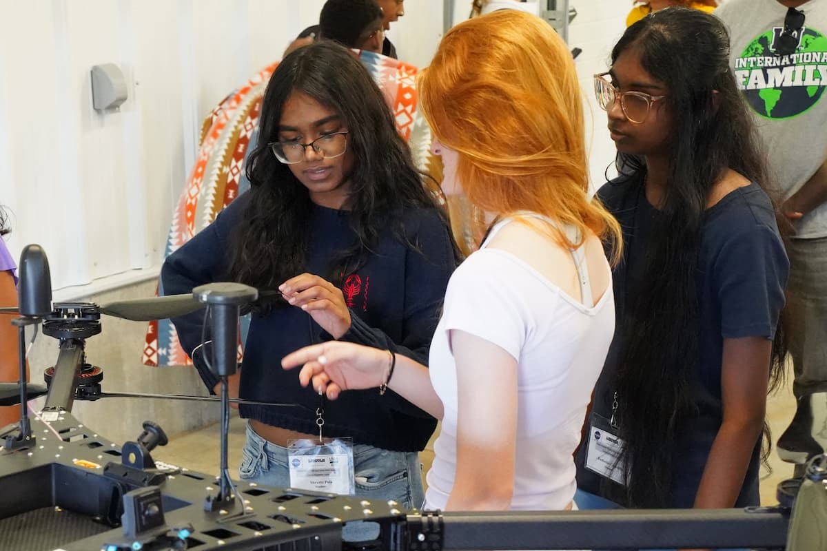 Three students look closely at a large drone and its components.