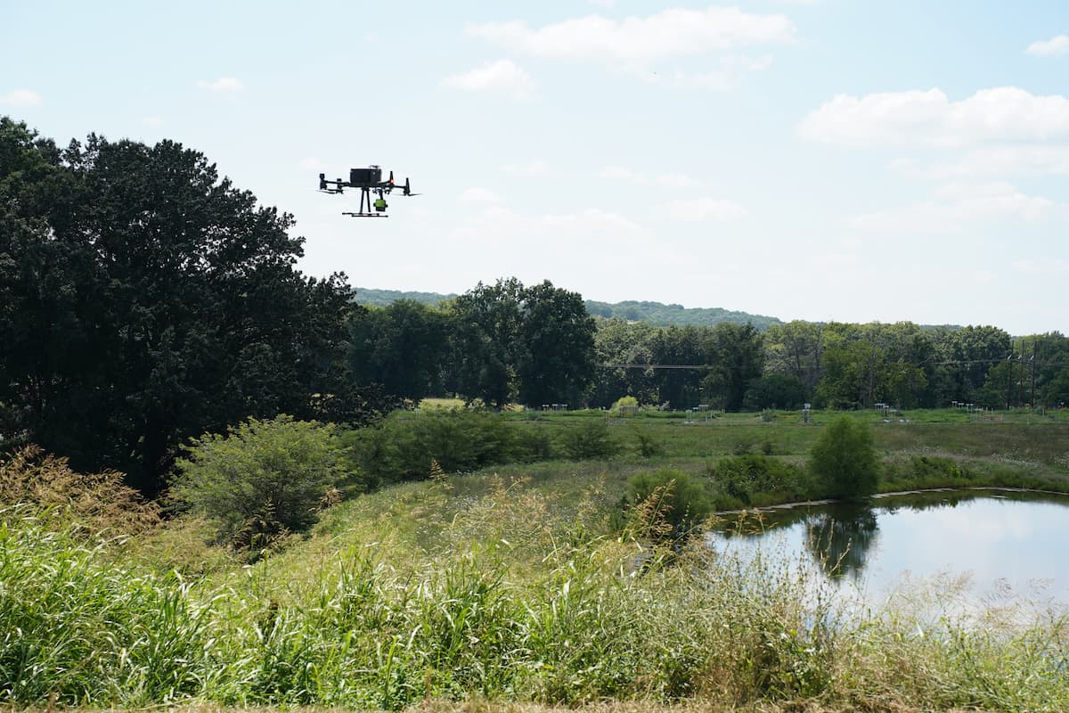 A drone flies above fields and a pond at Busby Farm.