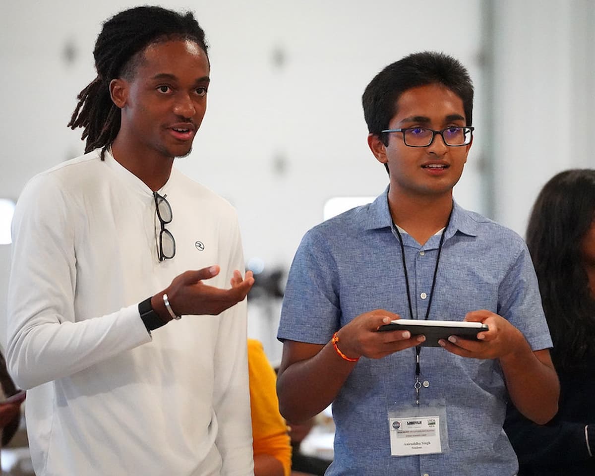 Two students discuss the activity while one holds a drone controller during a hands-on drone session.