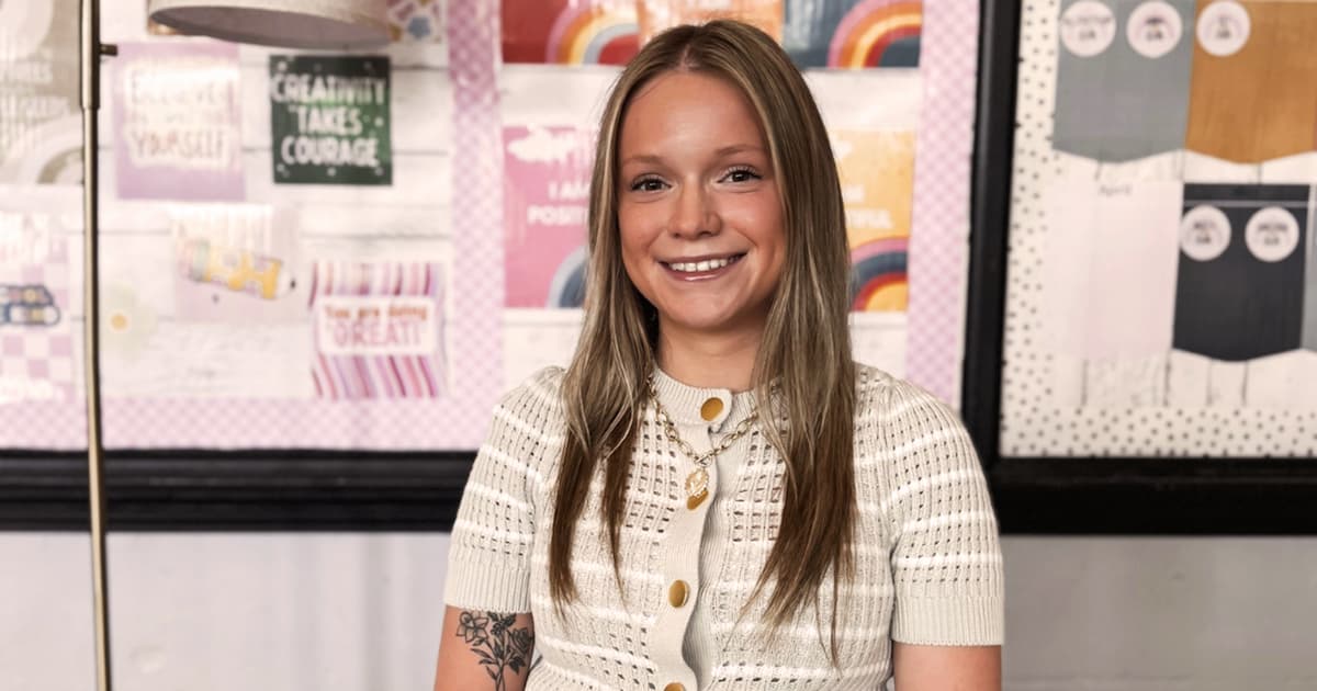 A young woman in a creme knit top smiles at the camera. 