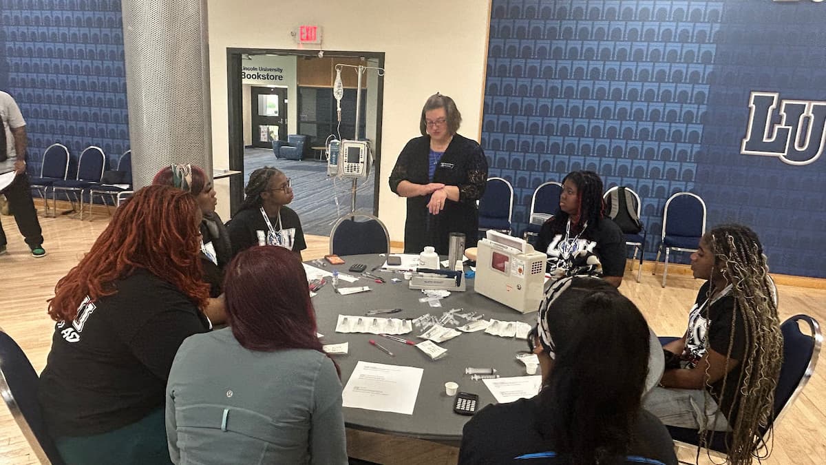 A group of students sit at a table filled with nursing school supplies.