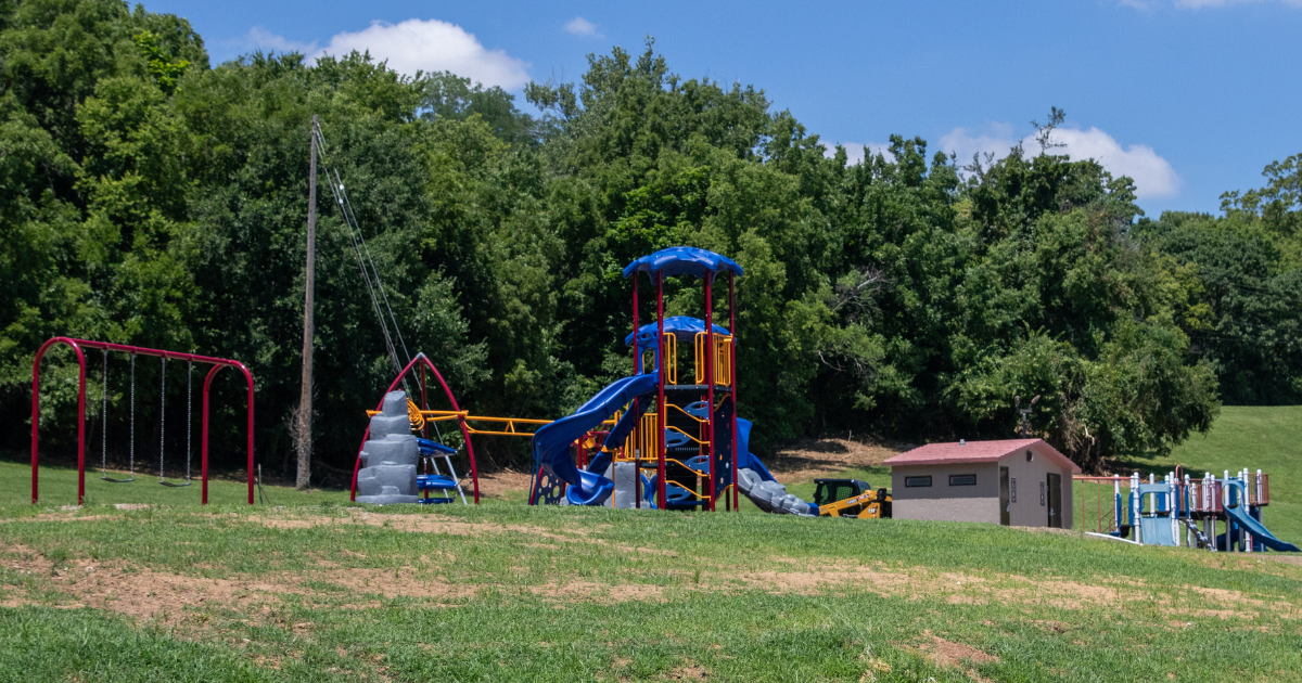 A children's play park with green grass, green trees and a blue sky. 