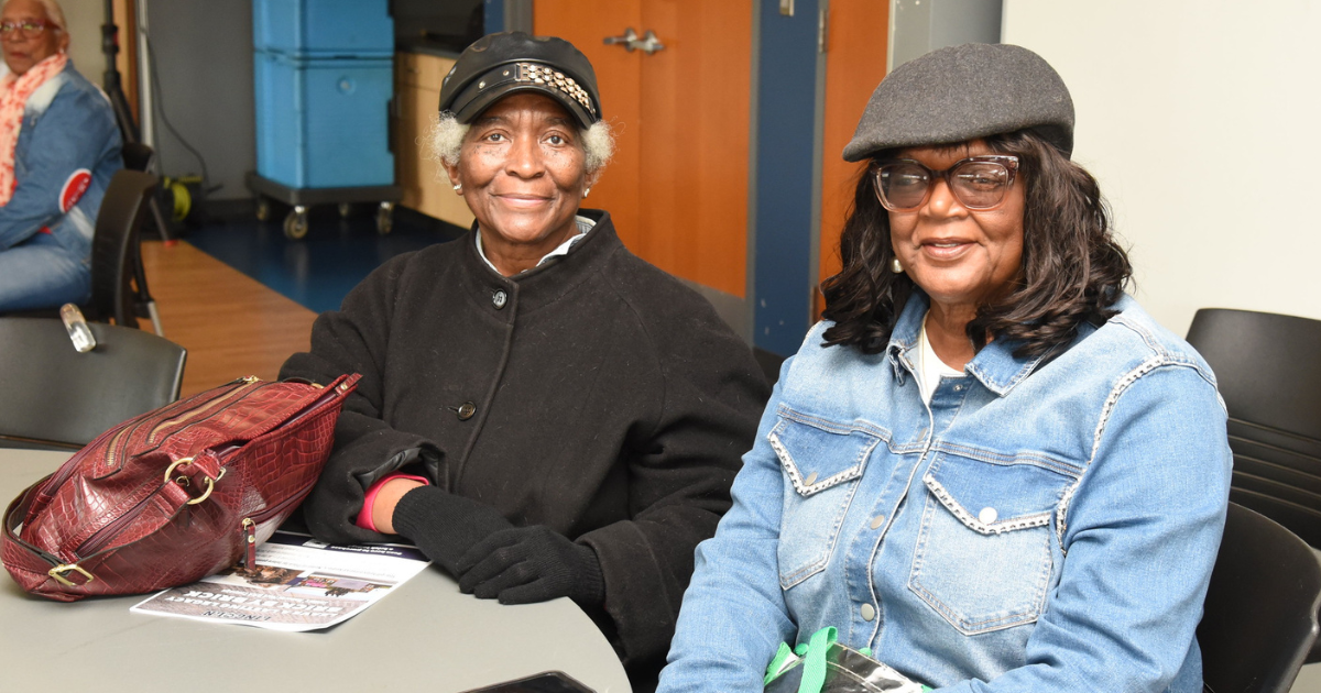 Two women sit at a table and smile for the camera.