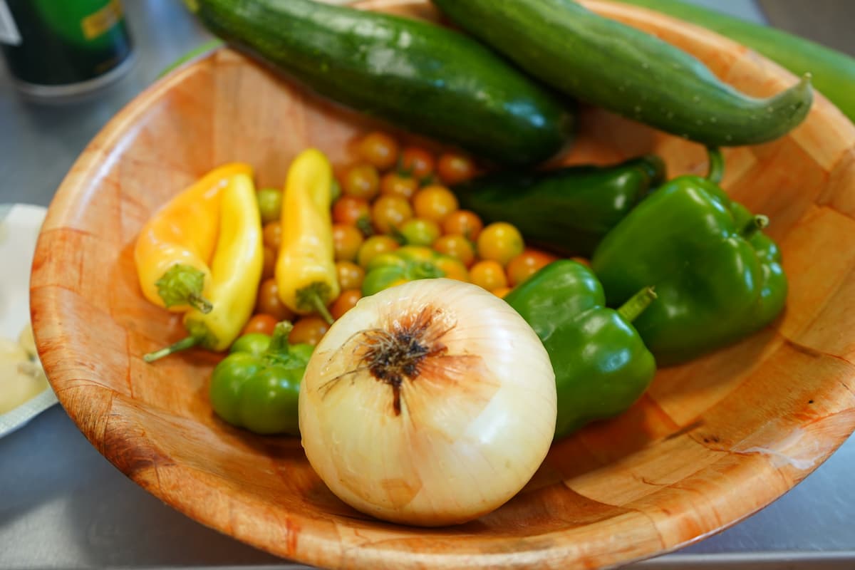 A wooden bowl holds onions, peppers, tomatoes and cucumbers used during the summer cooking series.