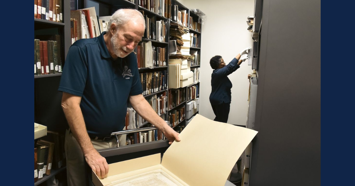 A man and a woman look through old materials in a workroom.