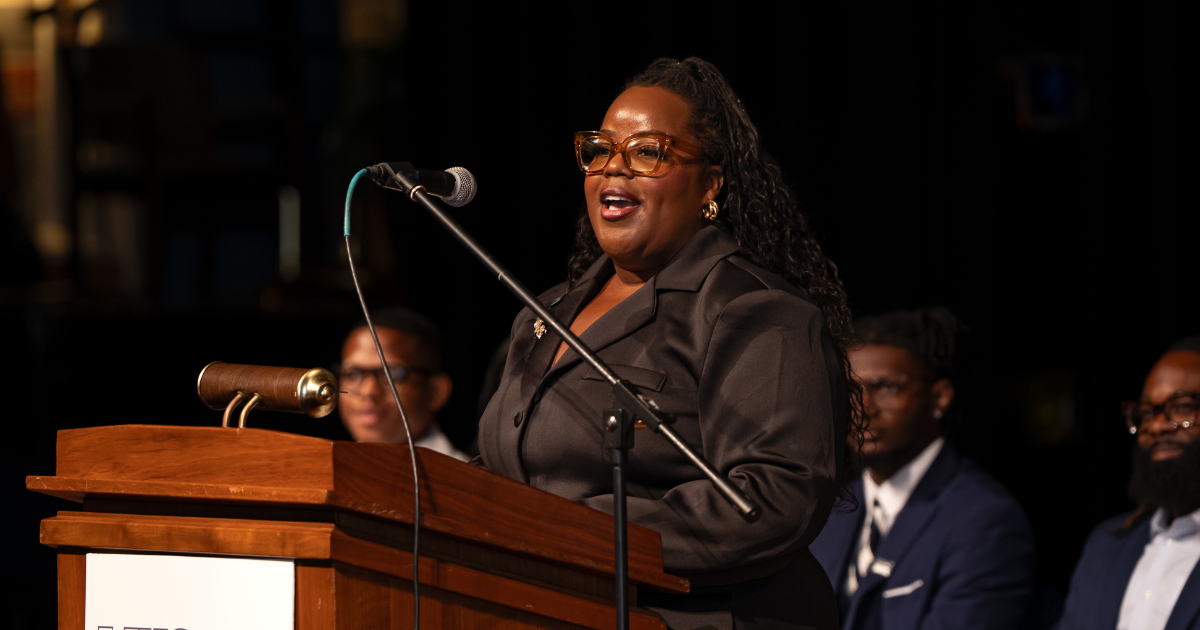 A woman stands behind a podium on a stage while giving a speech.