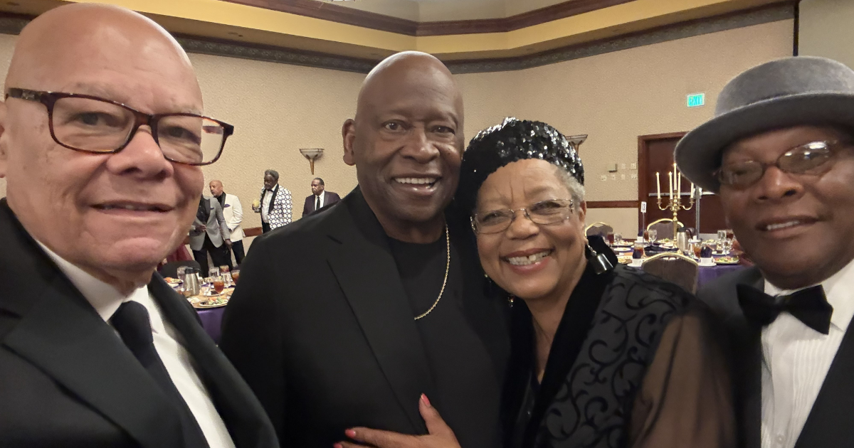 Four people dressed in black smile at the camera while in a banquet hall.