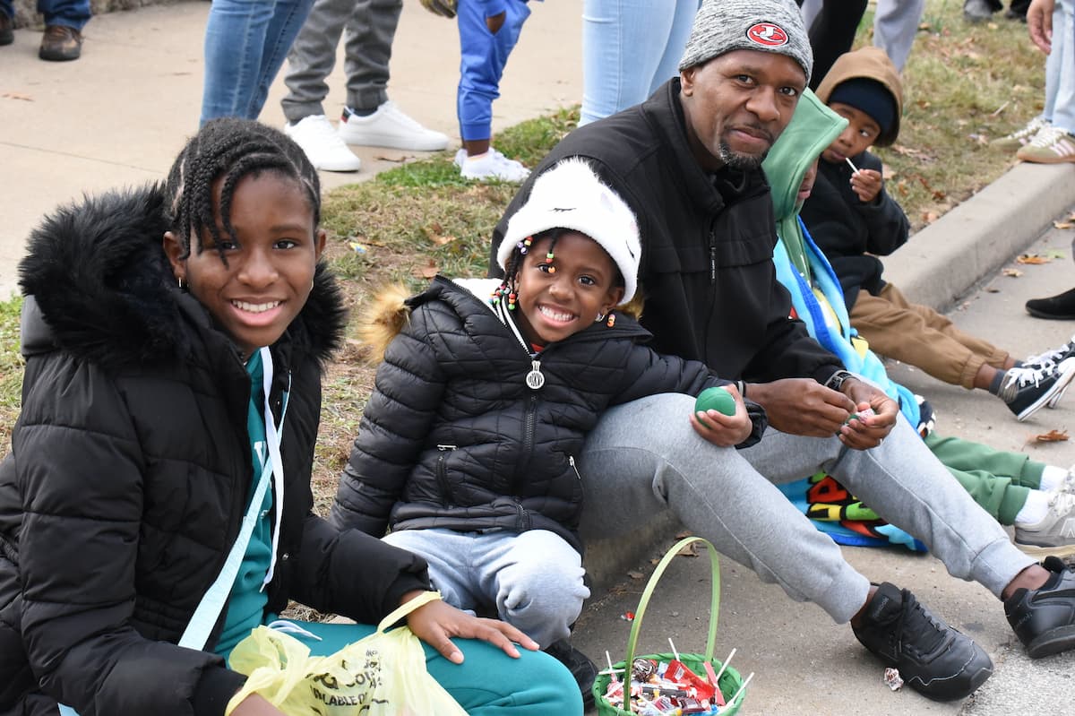 Two children and one adult male sit on the curb watching the 2025 Lincoln University Homecoming parade.