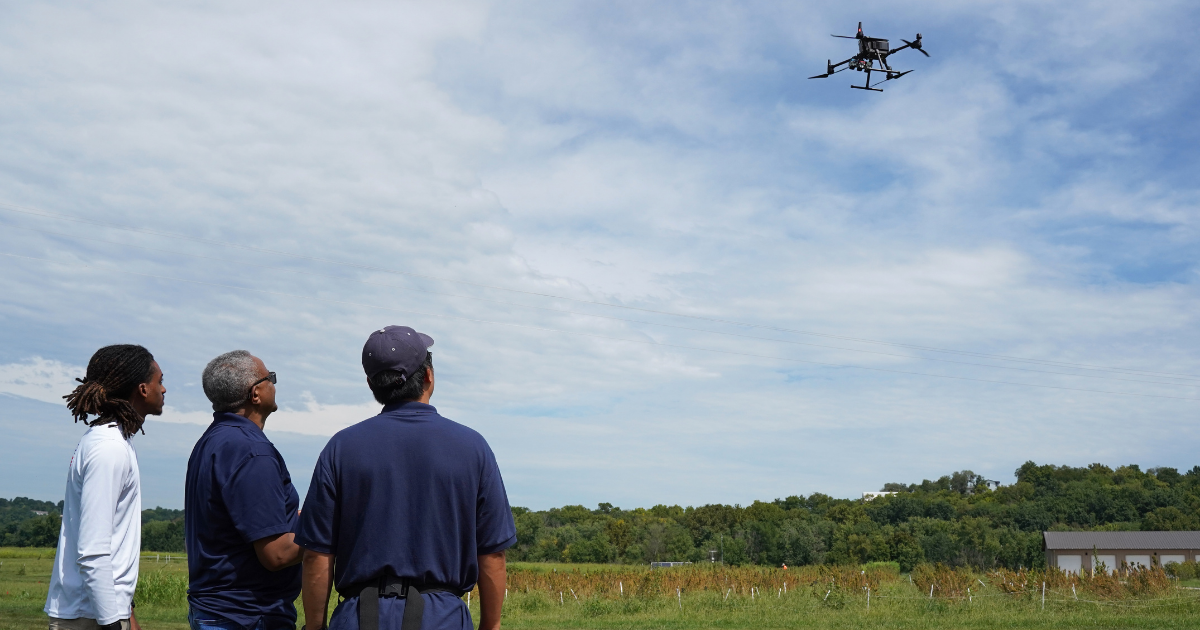 Three members of Lincoln University’s GIS team watch a drone fly above quinoa research plots at George Washington Carver Farm.