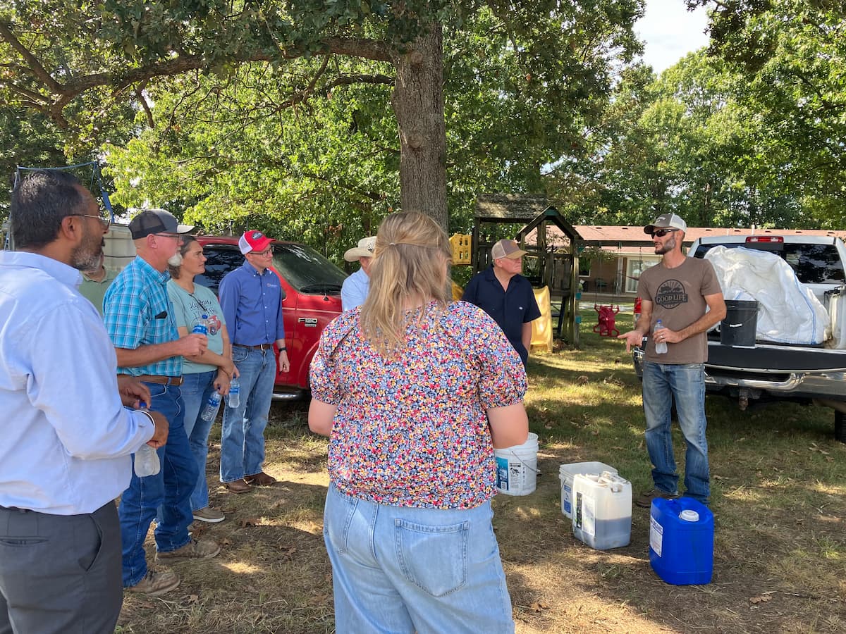 A small group of adults gathered outdoors beside pickup trucks and equipment.